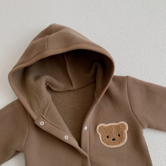Zoom sur la capuche et le patch ourson d’une combinaison bébé marron.