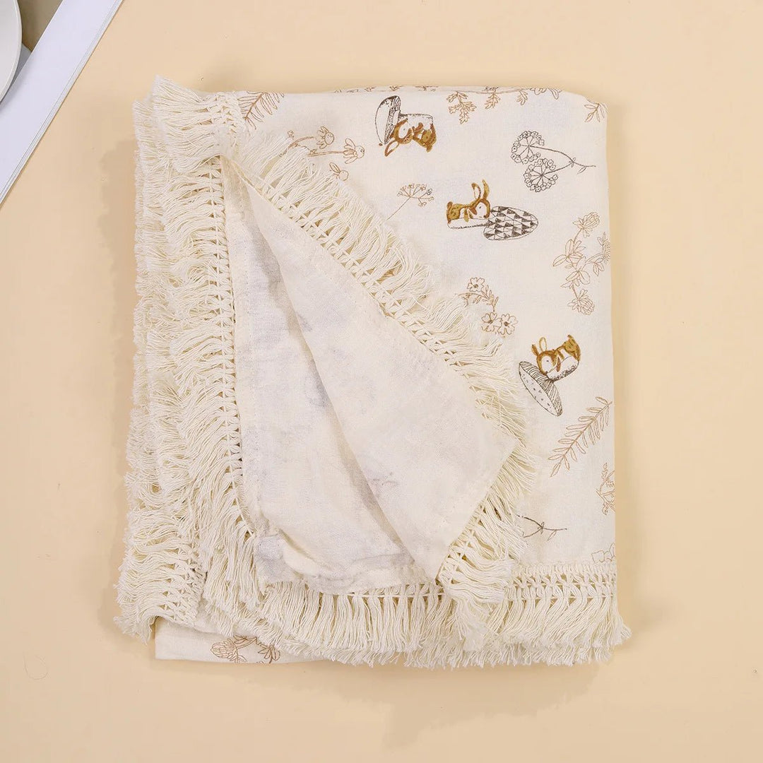 Couverture légère pour bébé Kalinatur, motif écureuils et feuillages beige, avec bordure à franges boho.
