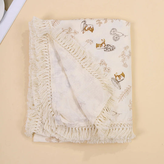 Couverture légère pour bébé Kalinatur, motif écureuils et feuillages beige, avec bordure à franges boho.
