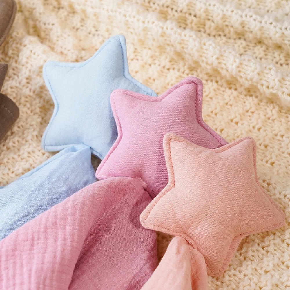 Lot de doudous étoile en gaze de coton rose, bleu et beige sur couverture