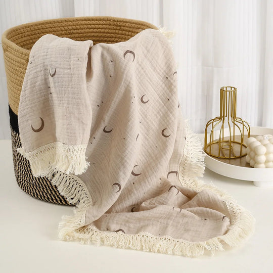 Lange bébé écru décoré de lunes avec franges, présenté dans un panier déco naturel.
