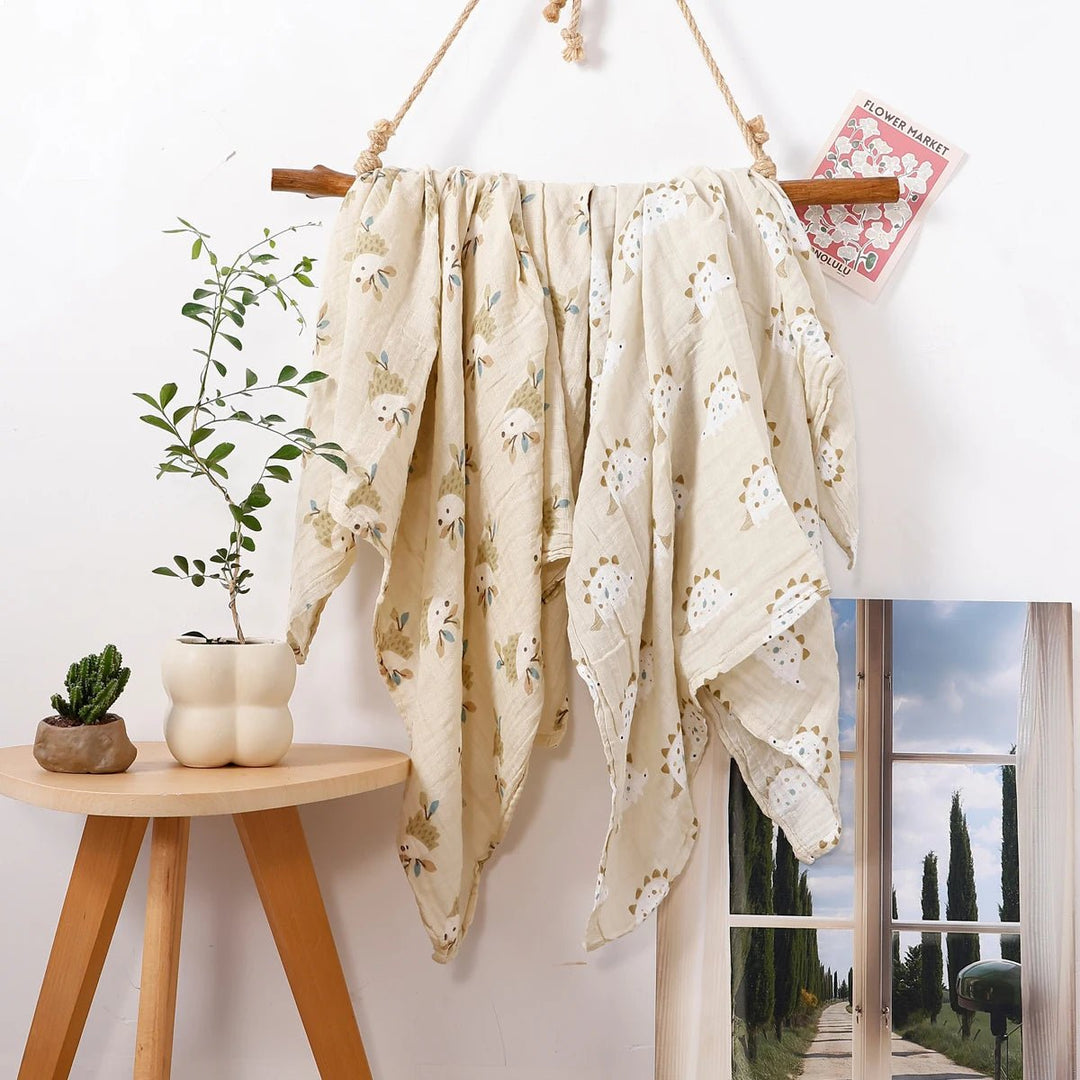 Lange en mousseline pour bébé avec motifs hérissons, suspendu sur un support en bois dans une décoration naturelle.