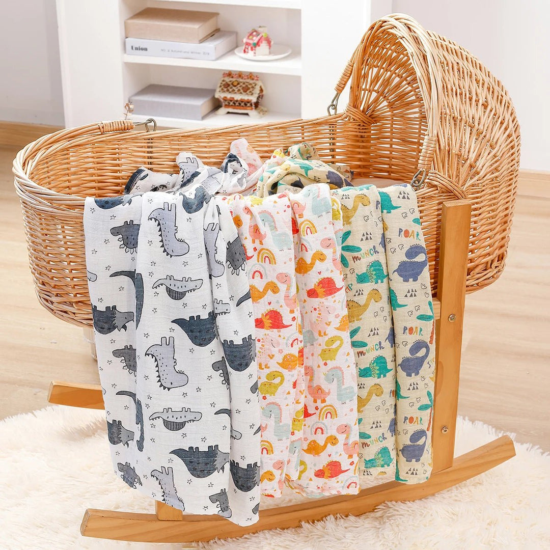 Langes en mousseline pour bébé décorés de motifs dinosaures colorés, suspendus sur un berceau en rotin dans un décor chaleureux.