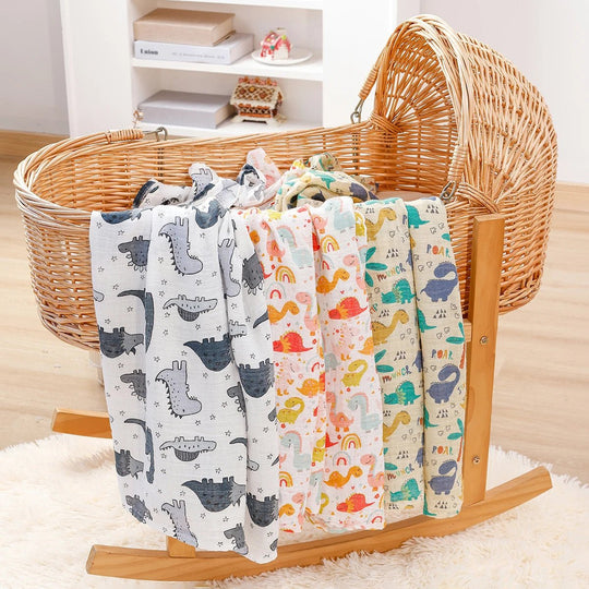 Langes en mousseline pour bébé décorés de motifs dinosaures colorés, suspendus sur un berceau en rotin dans un décor chaleureux.