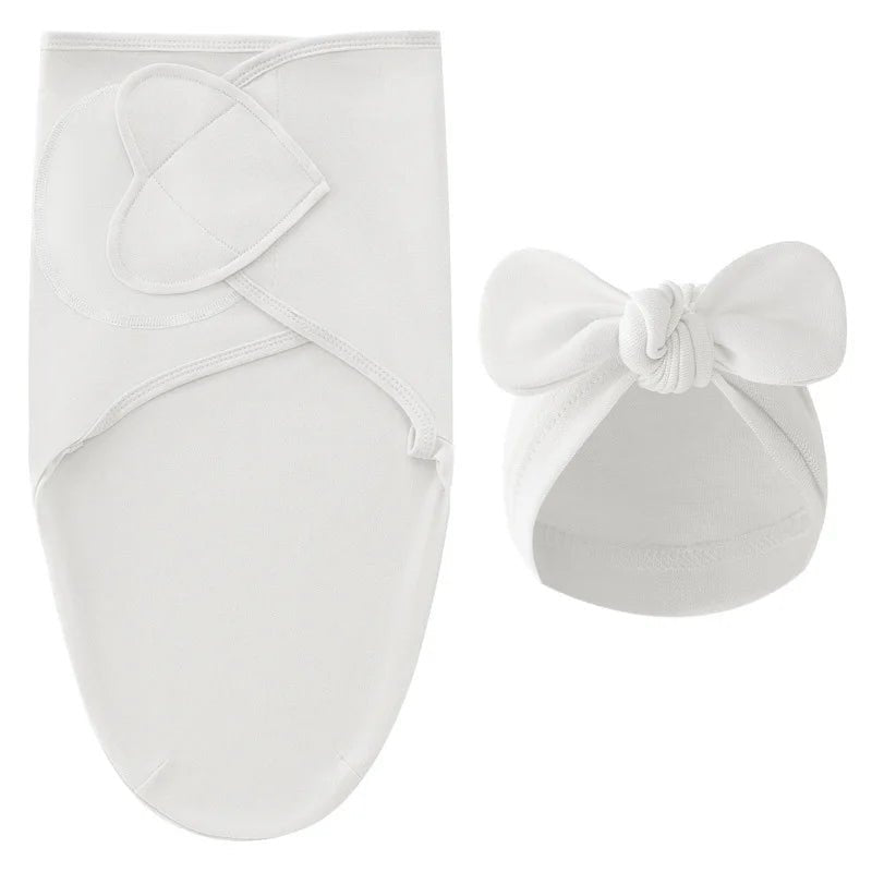 Nid d’ange blanc pour nouveau-né avec bonnet assorti à nœud, présenté sur fond clair.