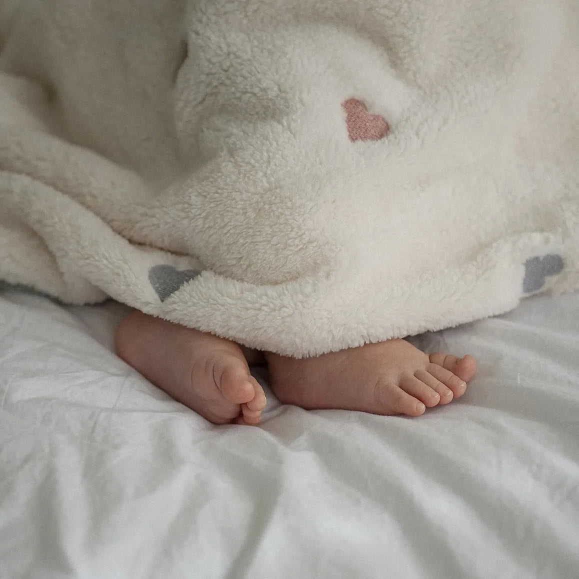 Petits pieds de bébé sous un plaid doux crème avec motif cœur rose Kalinatur