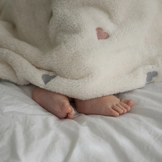 Petits pieds de bébé sous un plaid doux crème avec motif cœur rose Kalinatur