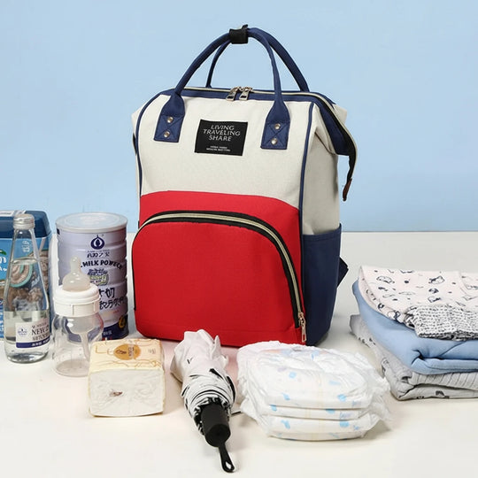 Sac à dos à langer Kalinatur rouge blanc et bleu présenté avec couches, biberons et accessoires bébé.