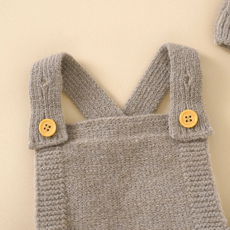 Détails des bretelles en tricot gris avec boutons en bois sur salopette bébé.