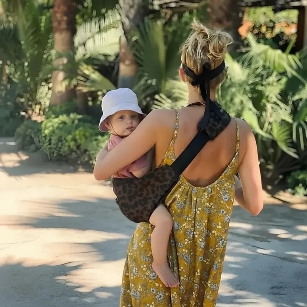 Maman portant son bébé avec un porte-bébé léopard ergonomique Kalinatur en promenade au soleil.