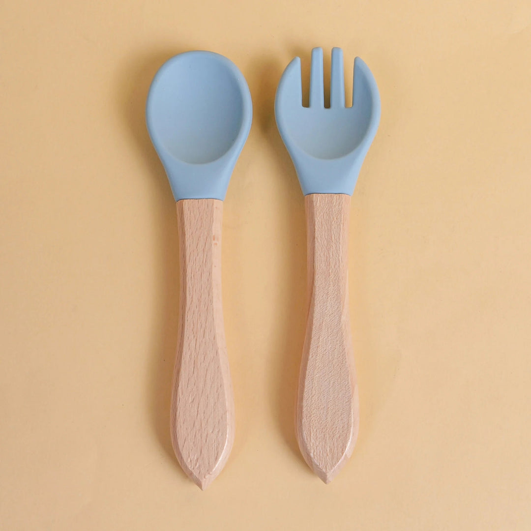 Set de cuillère et fourchette pour bébé en silicone bleu avec manche en bois naturel sur fond jaune
