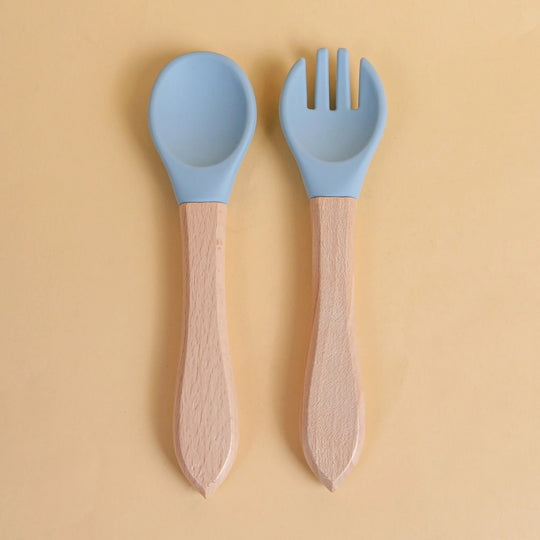 Set de cuillère et fourchette pour bébé en silicone bleu avec manche en bois naturel sur fond jaune
