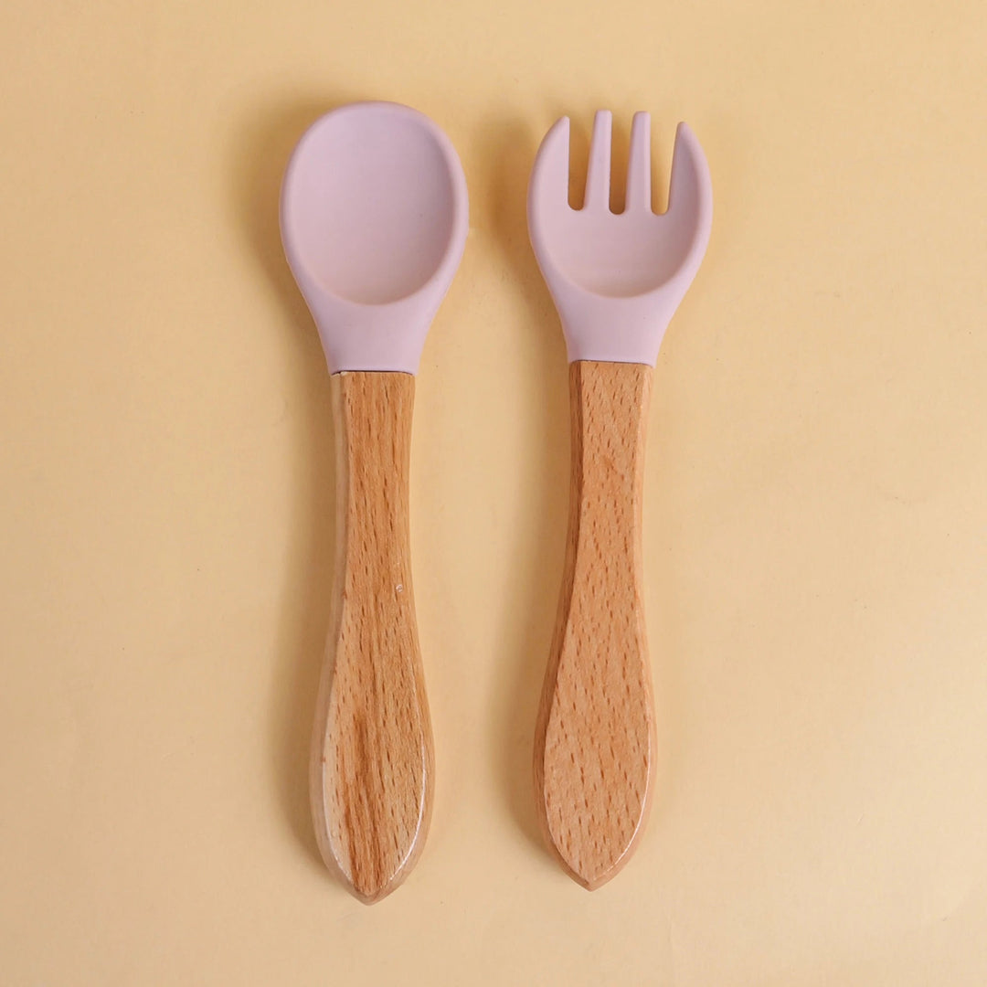 Set de cuillère et fourchette pour bébé en silicone violet avec manche en bois naturel sur fond beige
