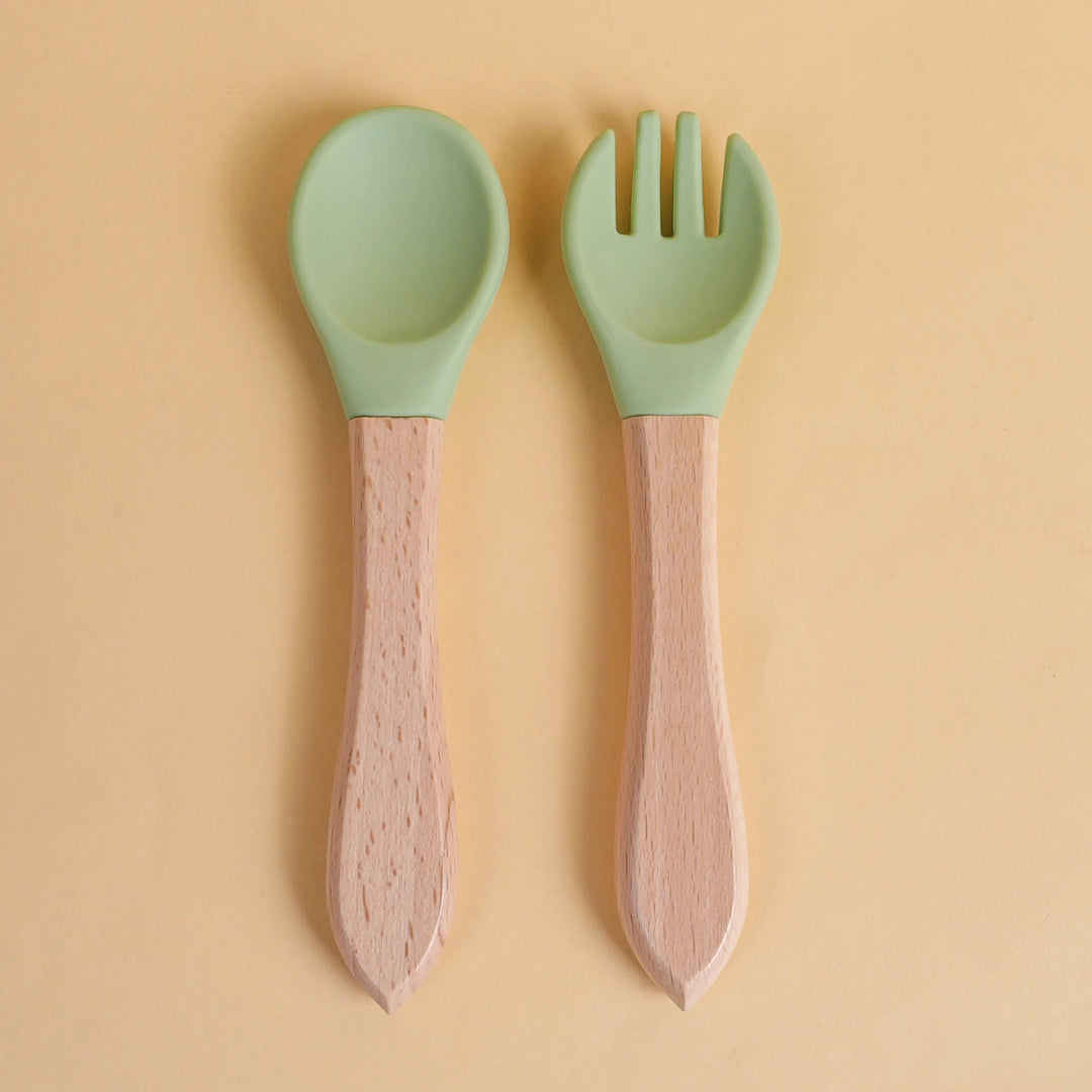 Set de cuillère et fourchette pour bébé en silicone vert avec manche en bois naturel sur fond beige
