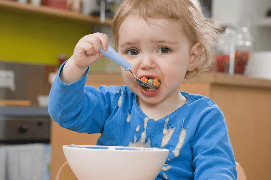 Bébé utilisant une cuillère en acier inoxydable avec manche ergonomique pour manger des légumes dans un bol