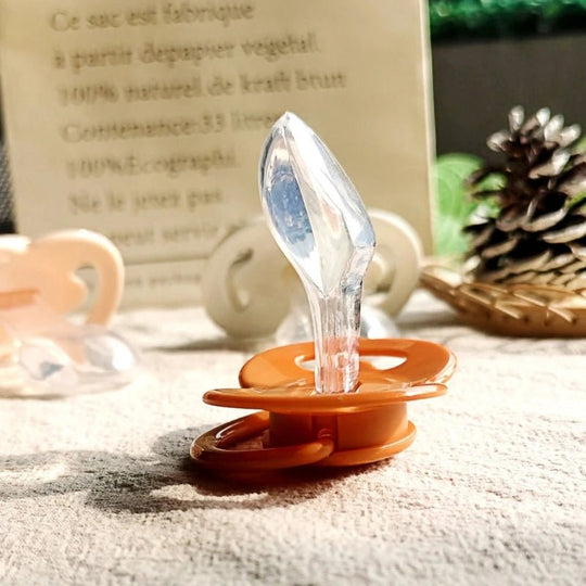 Tétine anatomique en silicone orange, présentation naturelle sur fond végétal – Kalinatur.